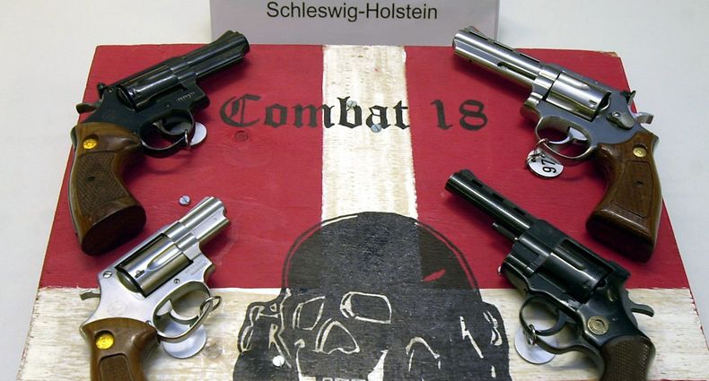 ARCHIV - 27.10.2003, Schleswig-Holstein, Kiel: Sichergestellte Waffen und ein Schild der kriminellen Neonazi-Gruppe «Combat 18» liegen im schleswig-holsteinischen Landeskriminalamt (LKA). (zu dpa Seehofer verbietet rechtsextreme Gruppe «Combat 18» - Festnahme) Foto: Horst Pfeiffer/dpa +++ dpa-Bildfunk +++