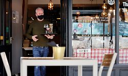 A worker wearing a face covering carries a customer's drinks order to their outside table at a re-opened restaurant in east London as coronavirus restrictions are eased across the country following England's third national lockdown on April 12, 2021. - Britons on Monday toasted a significant easing of coronavirus restrictions, with early morning pints -- and much-needed haircuts -- as the country took a tentative step towards the resumption of normal life. (Photo by Tolga Akmen / AFP)