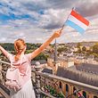 Happy traveler girl with Luxembourg flag and admiring the Grund from the observation deck.  Tourism, leisure and life in the country.