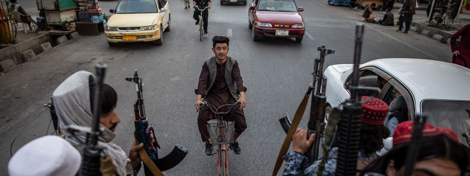 Ein Afghane fährt auf einem Fahrrad, während junge Taliban-Kämpfer auf der Ladefläche eines Pick-Ups in den Straßen von Kabul patrouillieren.
