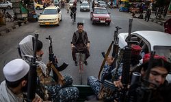 ARCHIV - 22.09.2021, Afghanistan, Kabul: Ein Afghane fährt auf einem Fahrrad, während junge Taliban-Kämpfer auf der Ladefläche eines Pick-Ups in den Straßen von Kabul patrouillieren. (zu dpa «Fragiler Frieden und zerstöre Träume: ein Jahr Taliban-Herrschaft») Foto: Oliver Weiken/dpa +++ dpa-Bildfunk +++