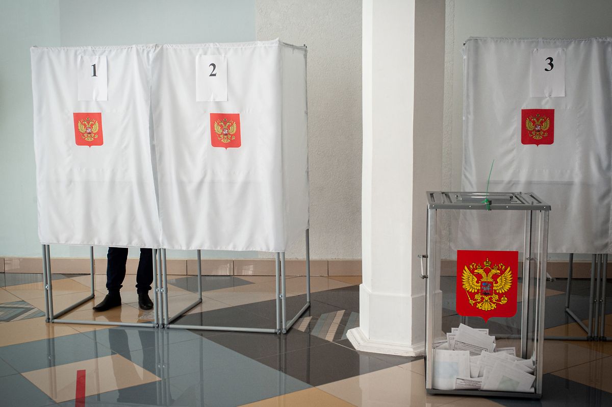 Eine Wahlurne mit dem Wappen der Russischen Föderation mit Stimmzetteln steht in einem Wahllokal.