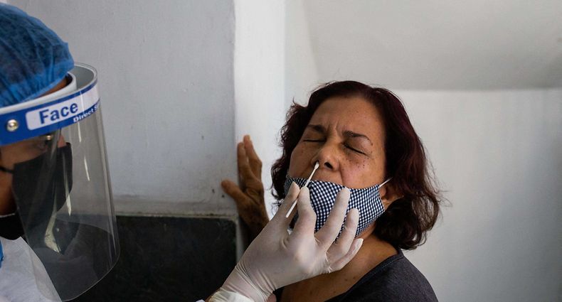 A municipal health worker takes a COVID-19 PCR test sample from a woman at the lobby of a residential building in Caracas, on January 22, 2022. (Photo by Cristian Hernandez / AFP)