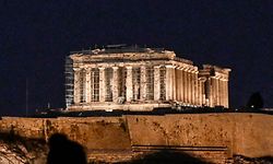 A woman is silhouetted as she takes picture of the illuminated Acropolis in Athens on August 1, 2022. - Greece will switch off floodlit monuments earlier as part of the EU measures to reduce energy and gas consumption after the summer. Before households are directly affected, municipalities will have to take the lamps out of 10% of their street lights and switch off lighting on monuments at 3 a.m. (Photo by Louisa GOULIAMAKI / AFP)