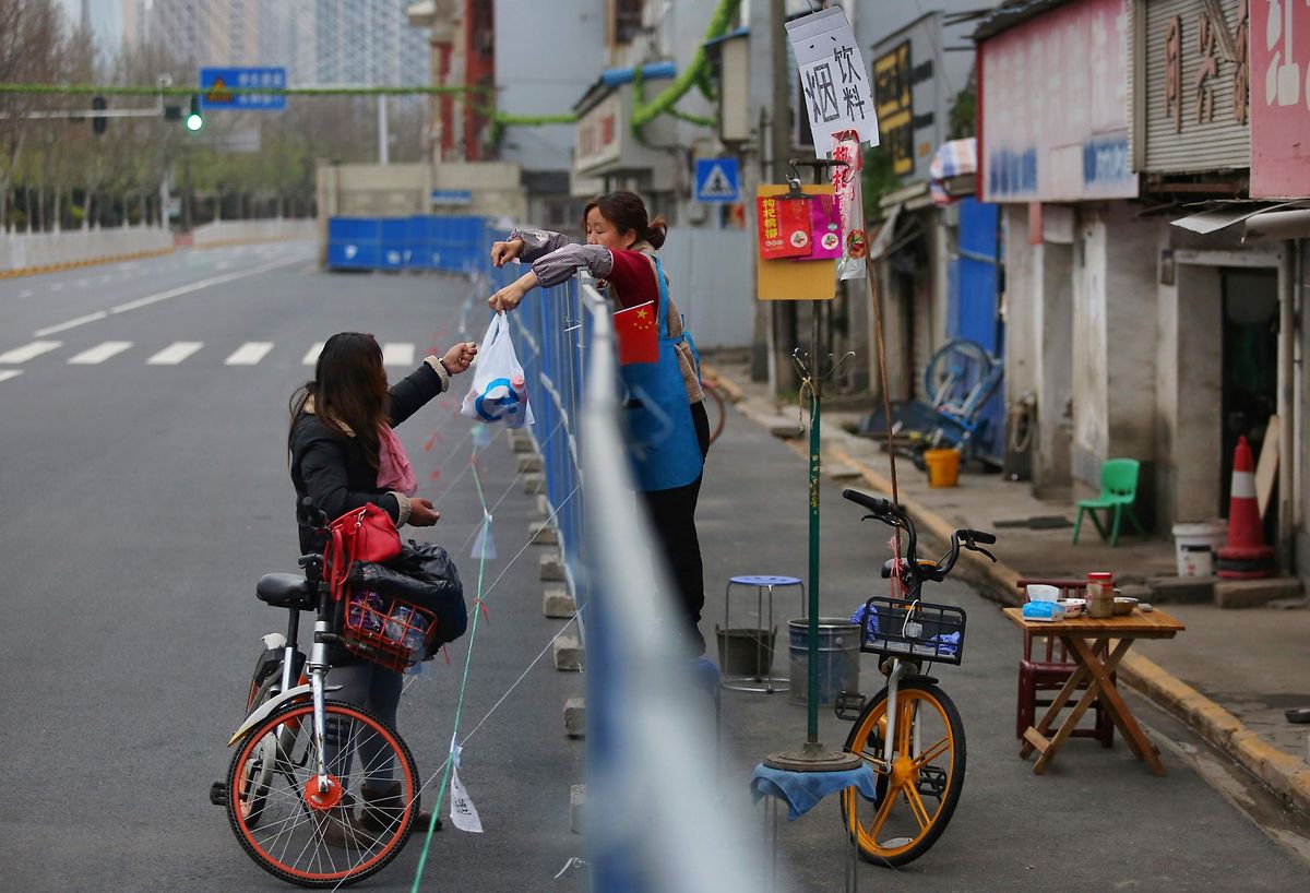 A woman delivers food to a resident over a barrier set up to prevent people entering or leaving a community in Wuhan Photo: AFP