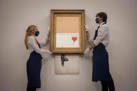 (FILES) In this file photo taken on September 3, 2021 assistants pose alongside an artwork titled �Love is the Bin� by British street artist Banksy during a photocall at Sotheby�s auction house in central London. - A partially shredded canvas of one of British artist Banksy's most celebrated works is expected to sell for millions when it goes under the hammer on October 14. (Photo by Tolga Akmen / AFP) / RESTRICTED TO EDITORIAL USE - MANDATORY MENTION OF THE ARTIST UPON PUBLICATION - TO ILLUSTRATE THE EVENT AS SPECIFIED IN THE CAPTION